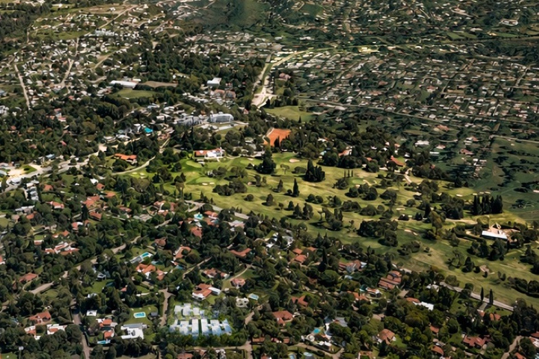 Vista aérea de Villa Allende Golf: la cancha en el medio, la casa de campo y las canchas de tenis a un costado, y el barrio con su arbolado alrededor.